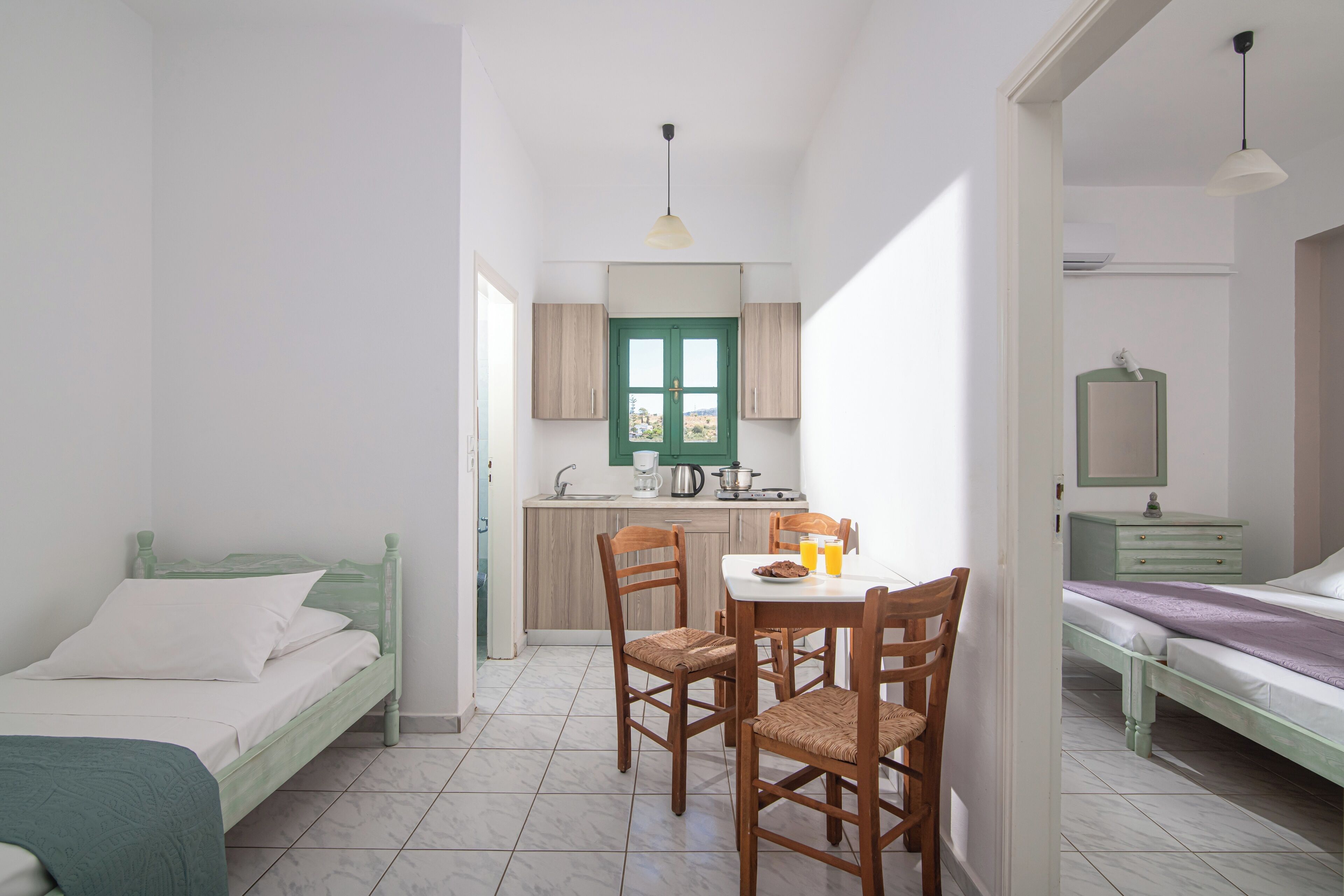 A compact room with a bed, a dining table with chairs, a kitchenette, and a small bathroom.