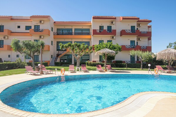 A swimming pool with lounge chairs and a building with balconies in the background. - Portokali Apartments (Hersonissos)