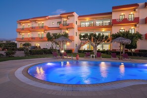 A hotel with a swimming pool, outdoor seating, and a well-lit building facade. - Portokali Apartments (Hersonissos)