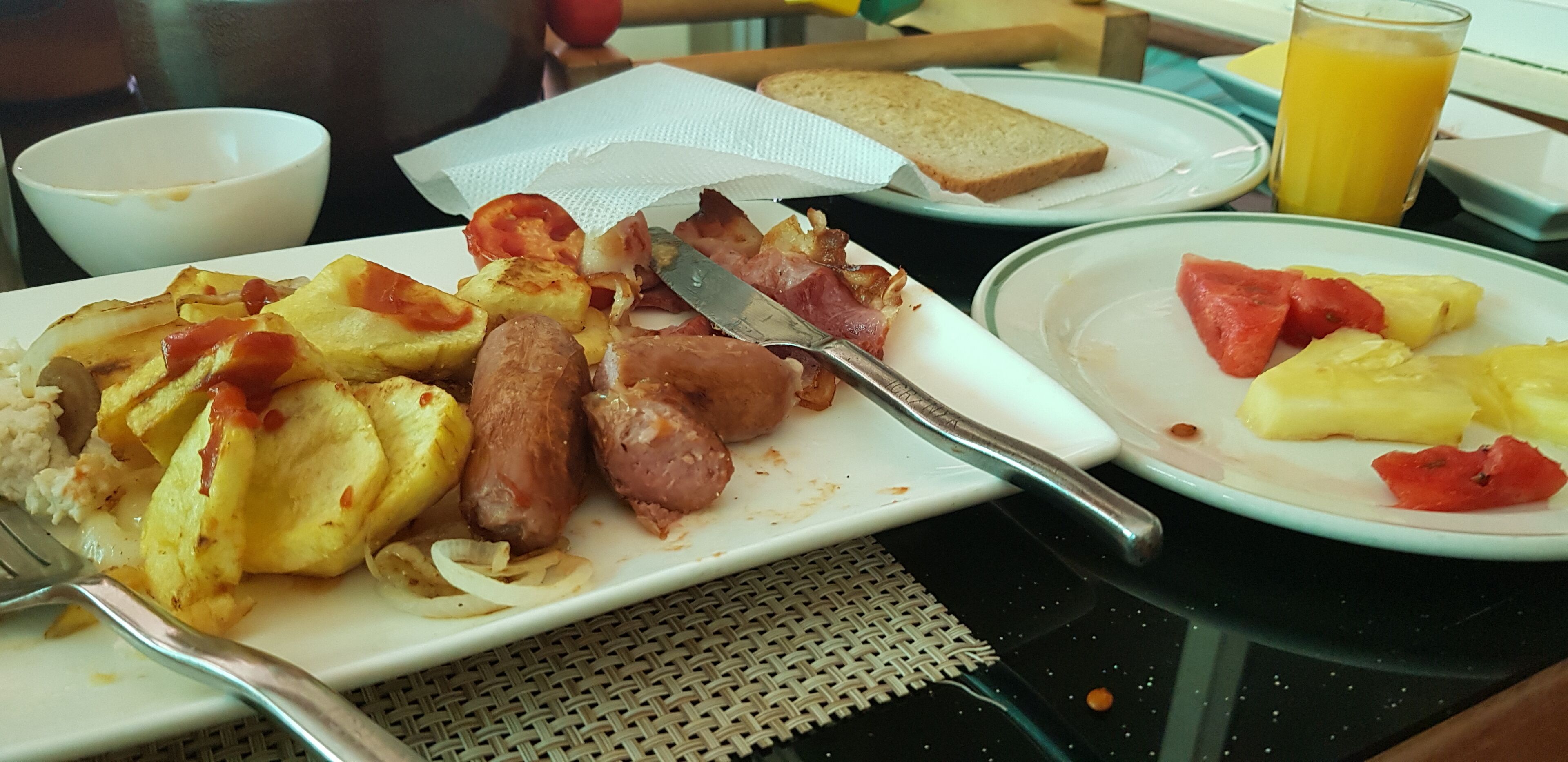 A breakfast setting with plates of food, a glass of orange juice, and a knife on a table.