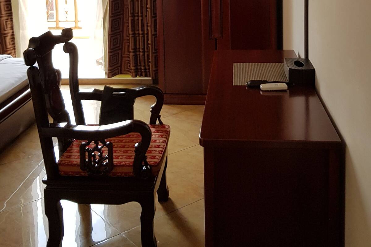 Une chambre d’hôtel avec un lit, une chaise en bois, un bureau avec une lampe et un téléviseur fixé au mur.