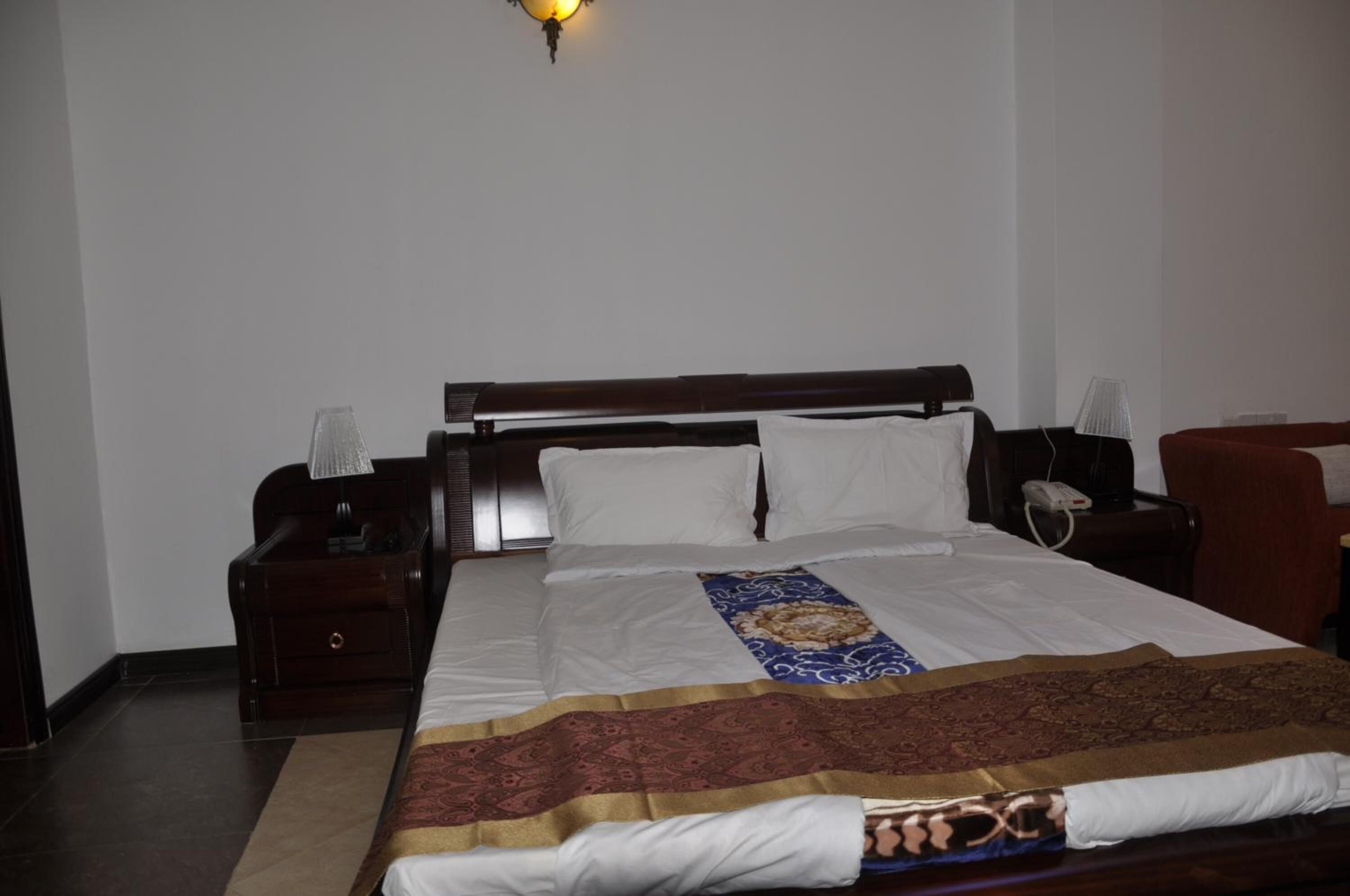 Habitación de hotel con una cama grande, cabecera de madera, mesita de noche con lámpara y teléfono.