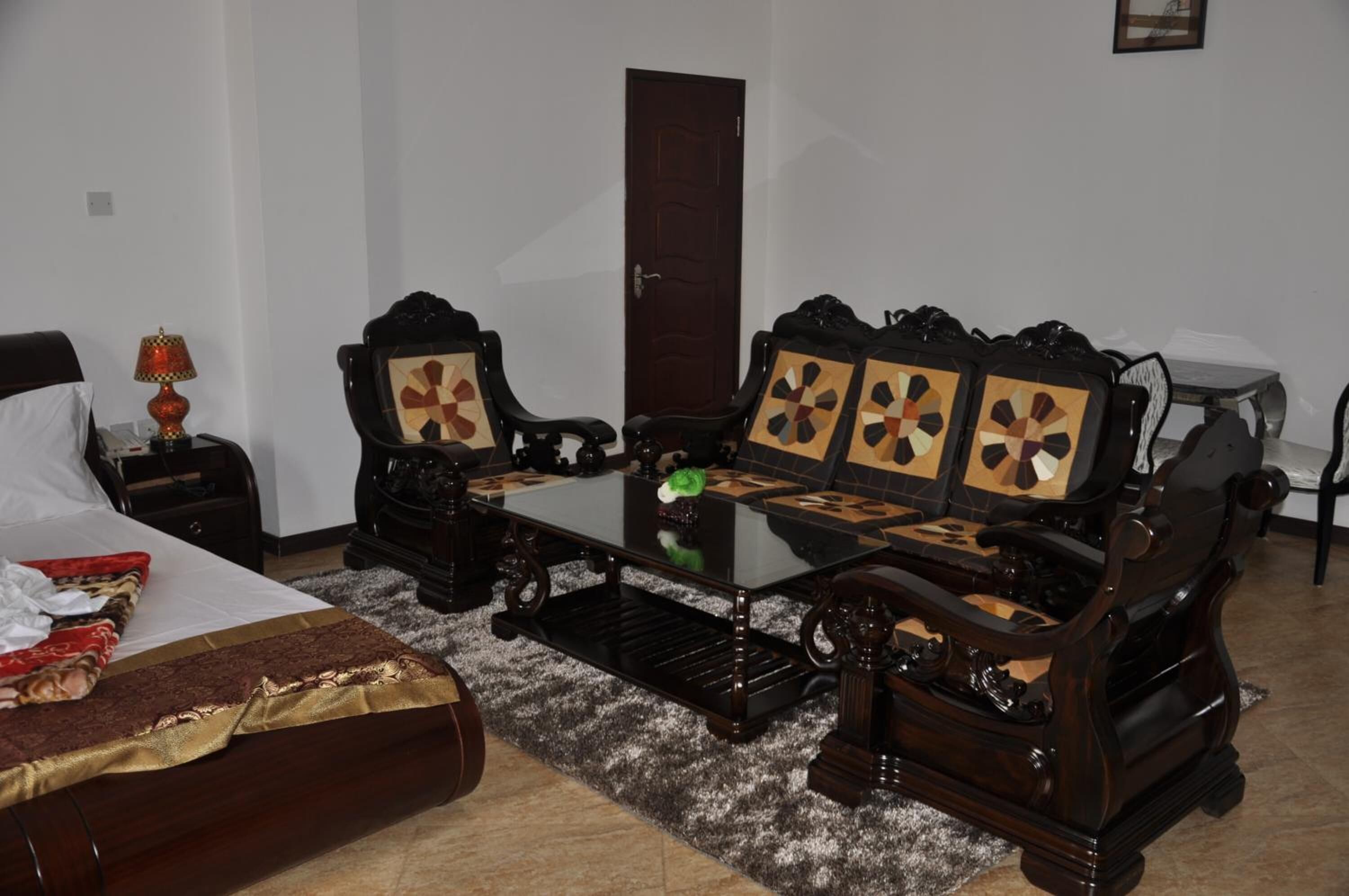 A room with a bed, a table, two chairs, a lamp, and a door.