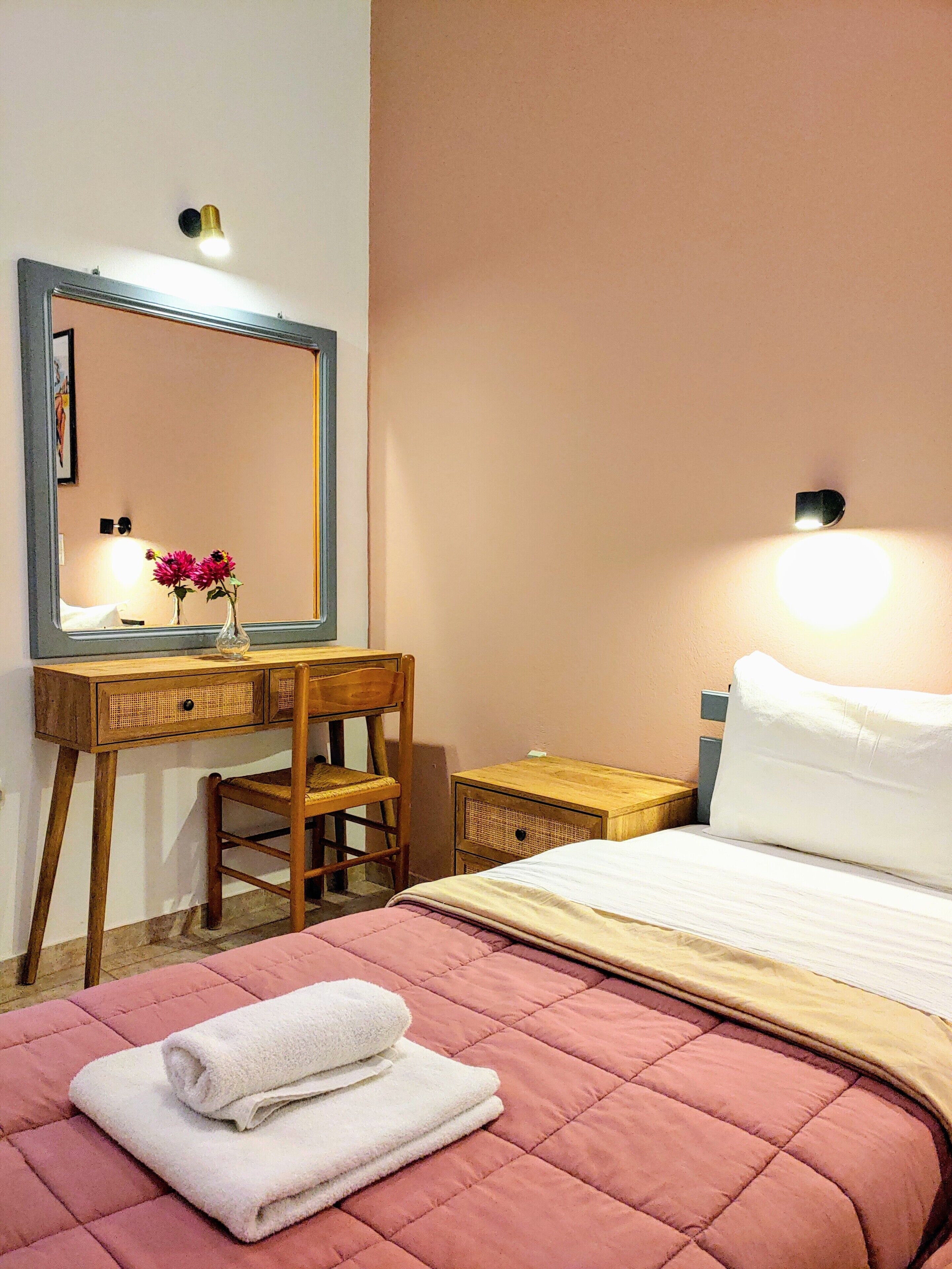 A bedroom with a bed, a wooden desk, a chair, a mirror, and a bedside table.