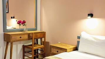 A bedroom with a bed, a wooden desk, a chair, a mirror, and a bedside table.