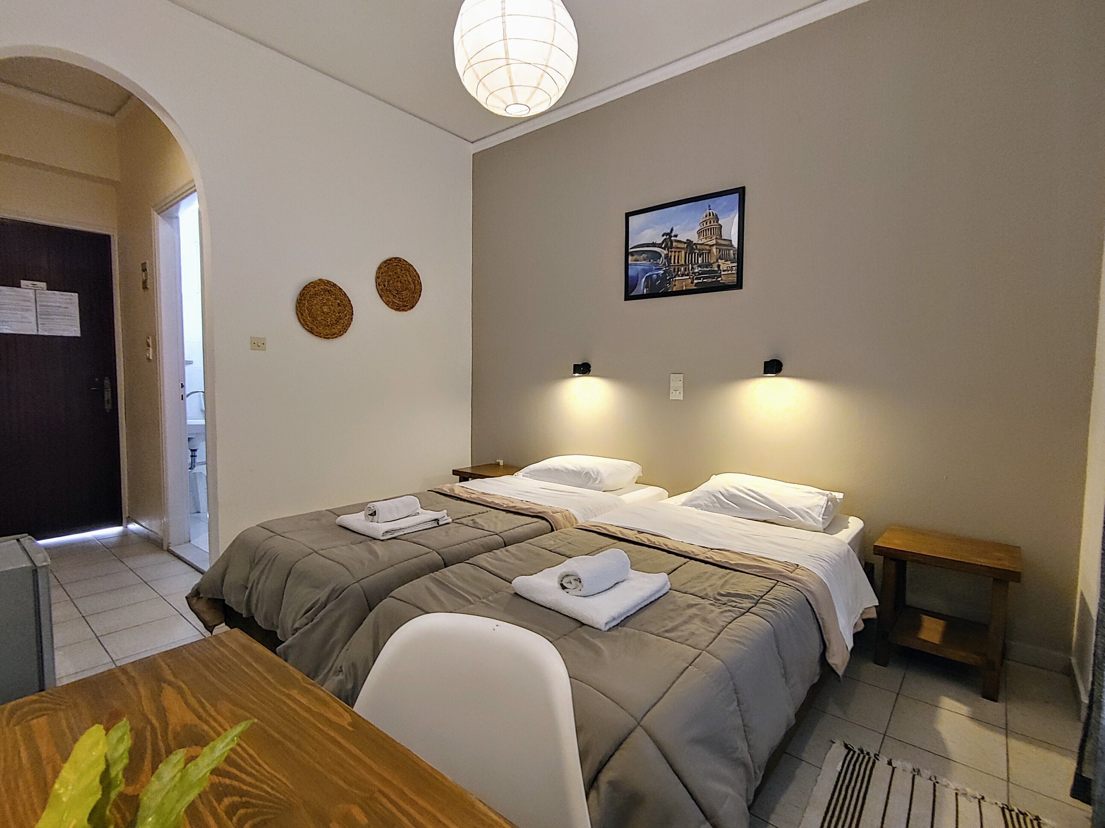 Ein Hotelzimmer mit zwei Betten, einem Holztisch, einem kleinen Nachttisch und einem an der Wand hängenden Bild.