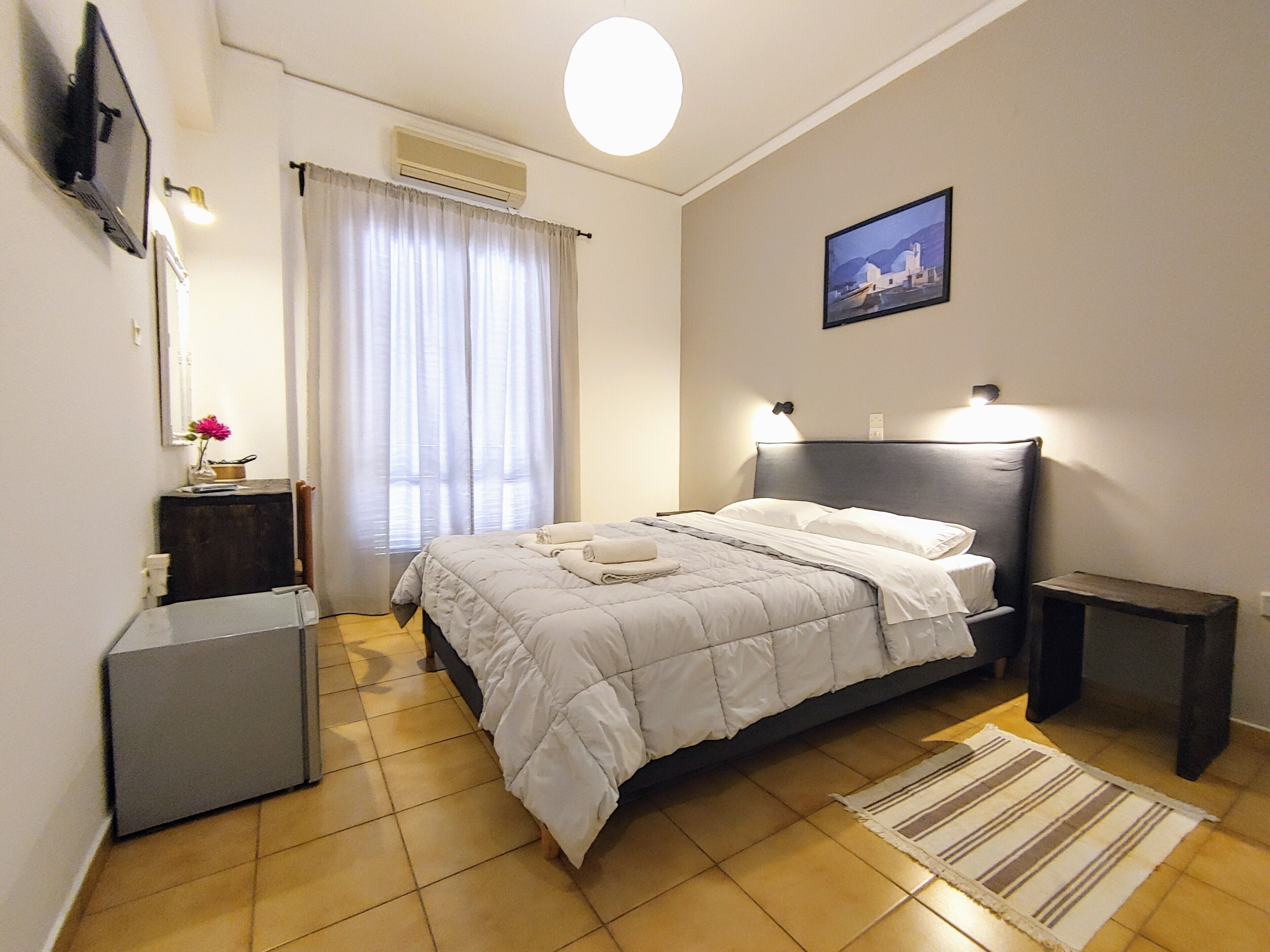 A hotel room with a bed, bedside tables, a desk, a chair, a lamp, a picture on the wall, and a window with curtains.