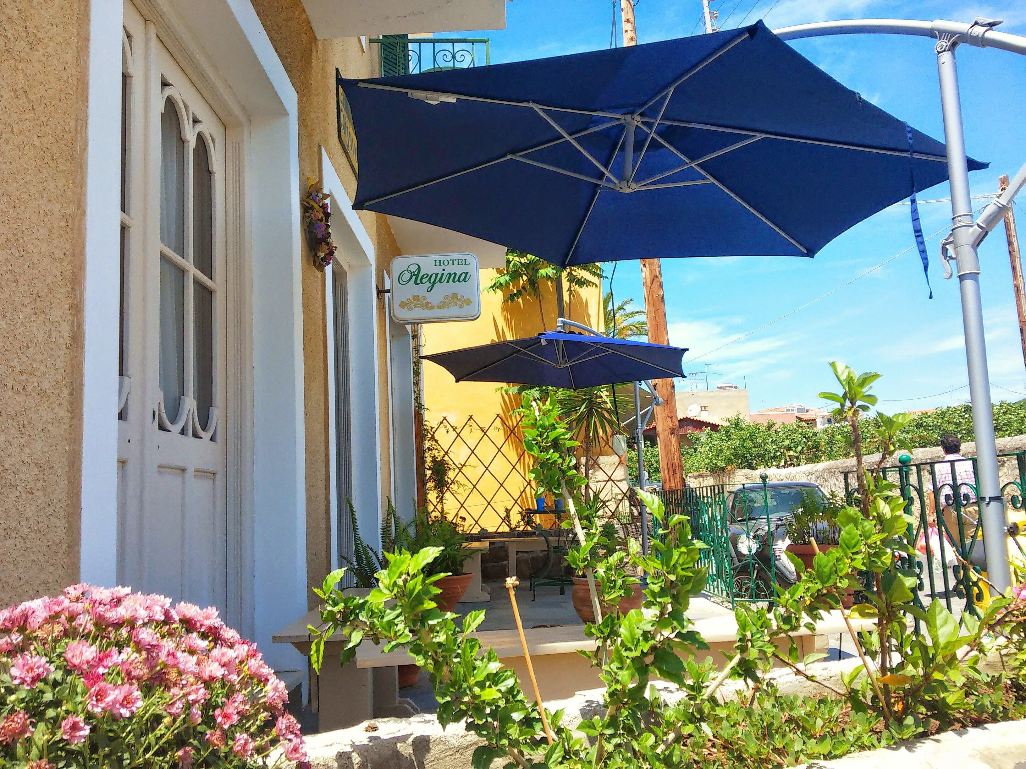 A hotel entrance with a sign reading "Hotel Regina," outdoor seating with umbrellas, and potted plants.