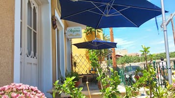 A hotel entrance with a sign reading "Hotel Regina," outdoor seating with umbrellas, and potted plants.