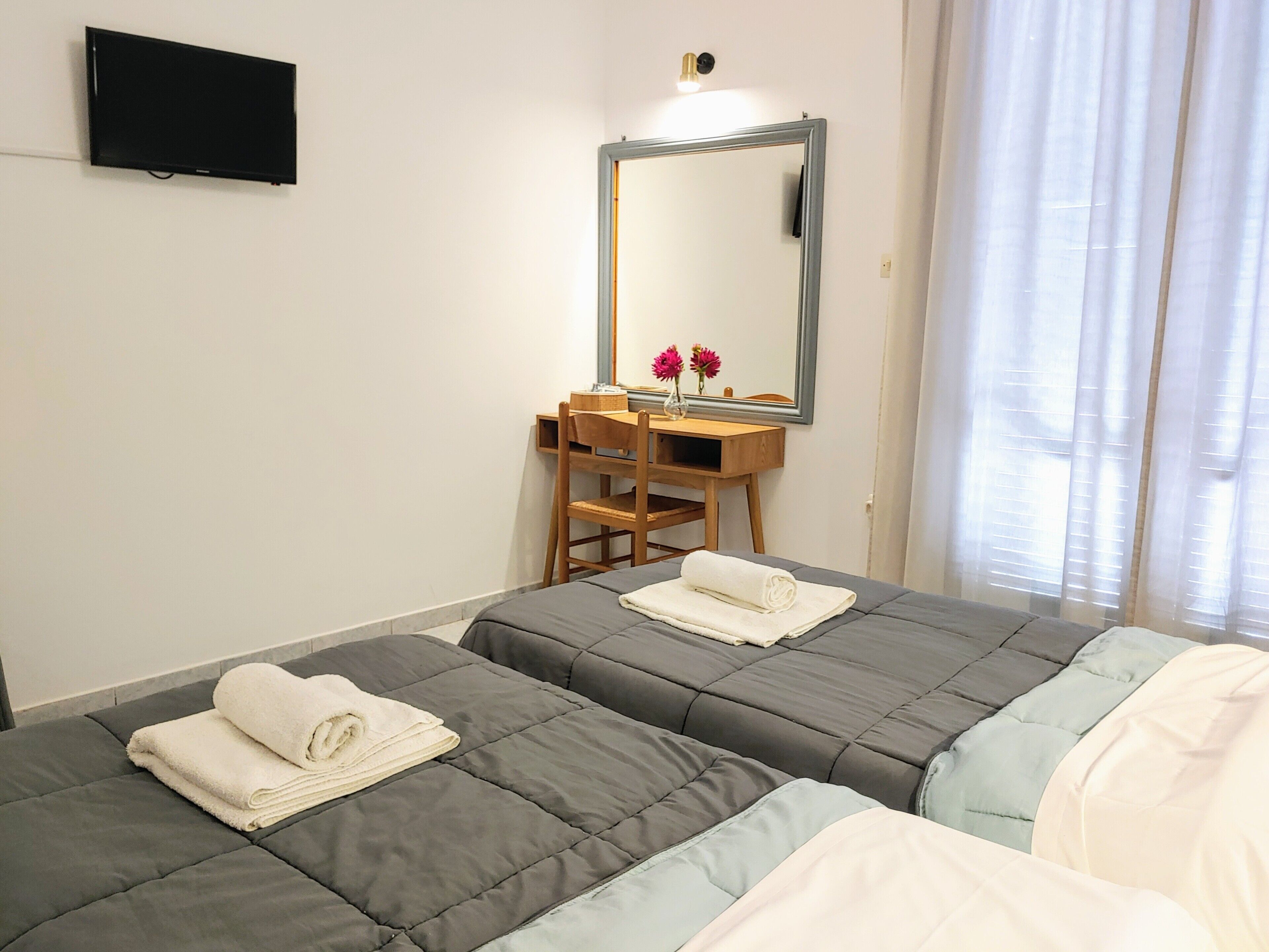 Quarto de hotel com duas camas, uma escrivaninha, um espelho e uma televisão.