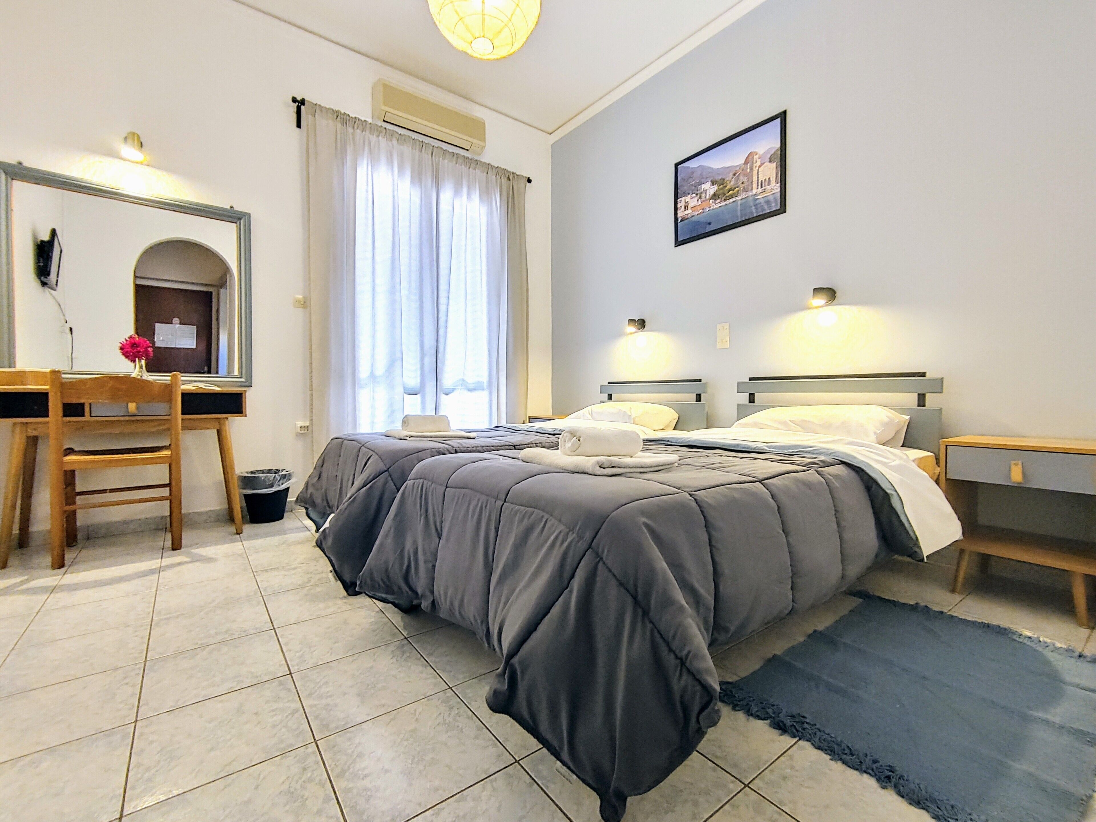 A bedroom with a bed, bedside tables, a desk with a chair, a mirror, and a window with curtains.