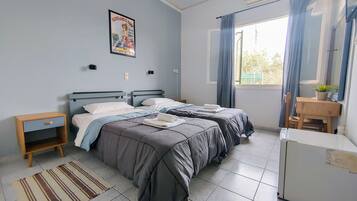 A bedroom with two beds, a small desk, a refrigerator, a window with curtains, and a poster on the wall.