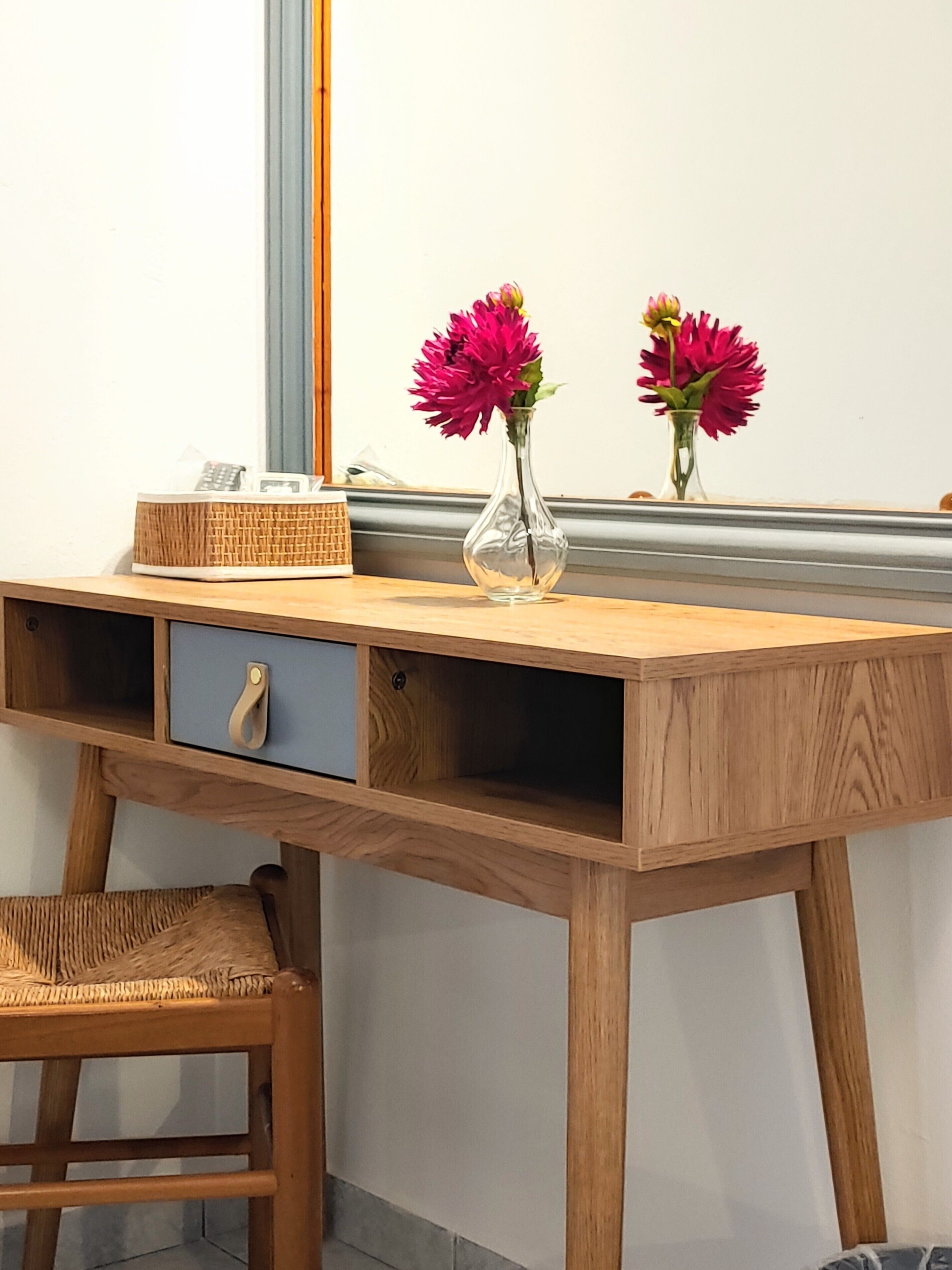 Un escritorio de madera con un jarrón de flores, una cesta de mimbre y una silla.