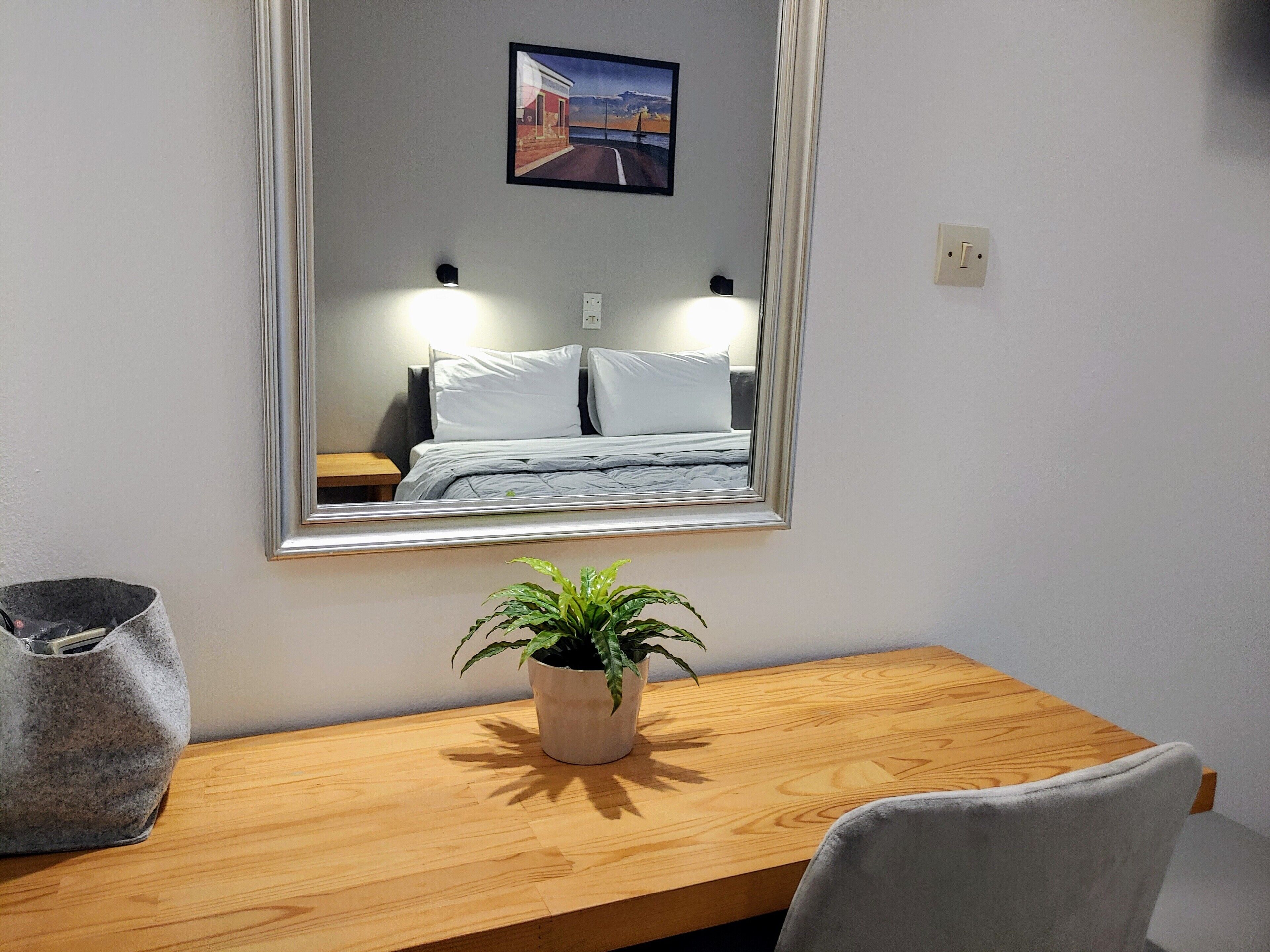 A bedroom with a bed, bedside tables, a mirror, a potted plant, a wooden desk, and a chair.