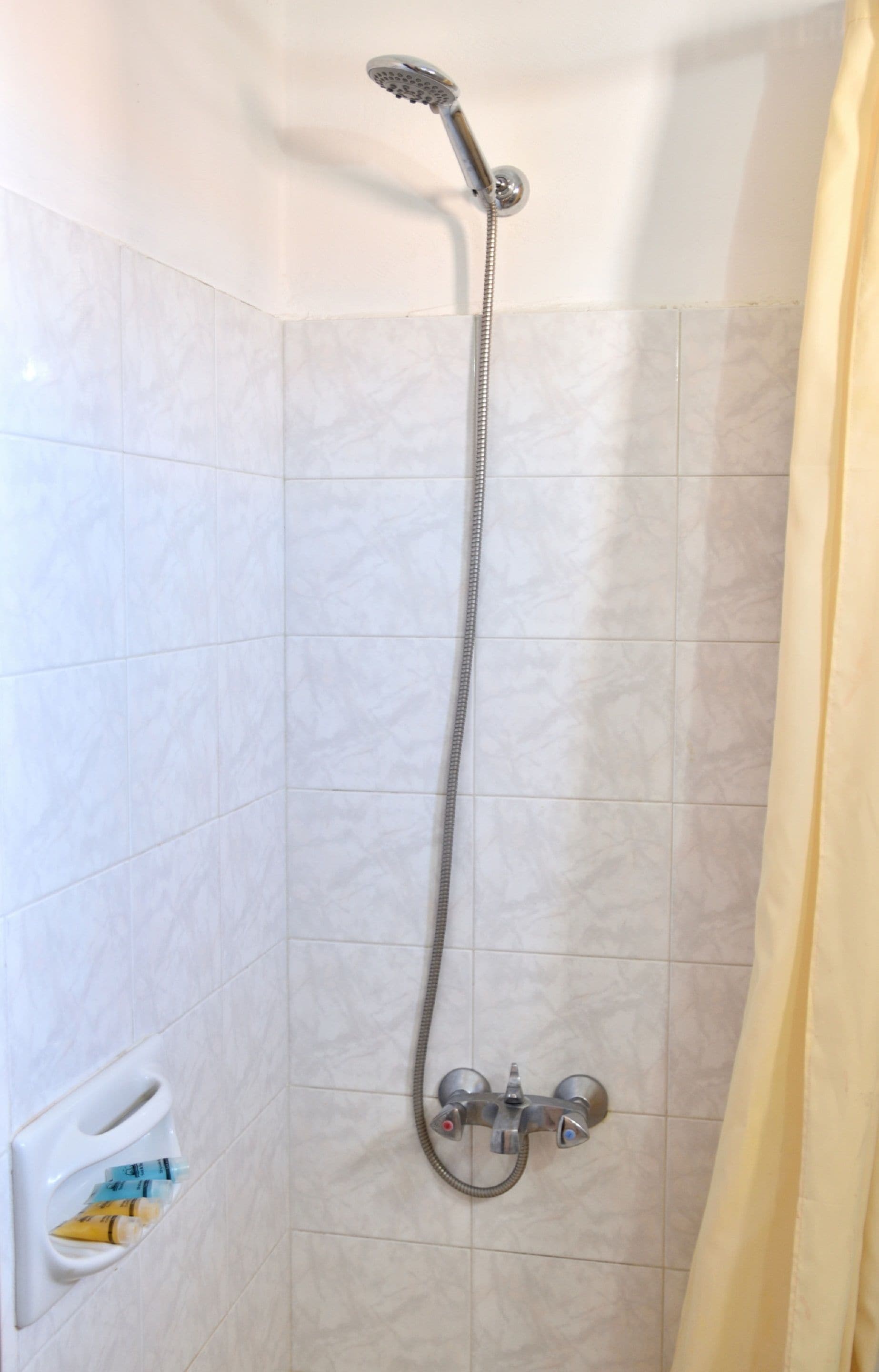 A shower with a handheld showerhead and a wall-mounted faucet.