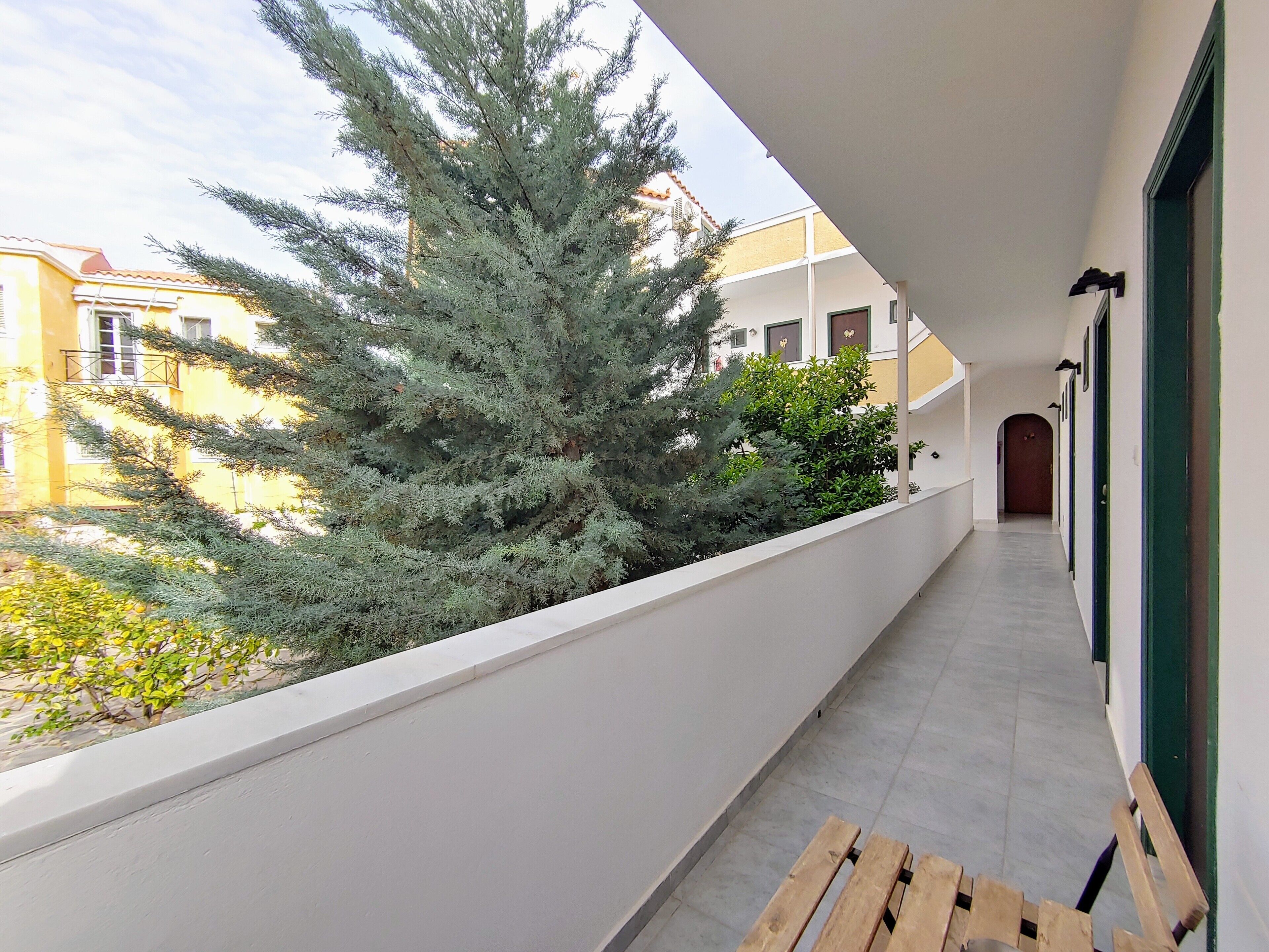 A balcony with a wooden bench, a potted plant, and a view of neighboring buildings.