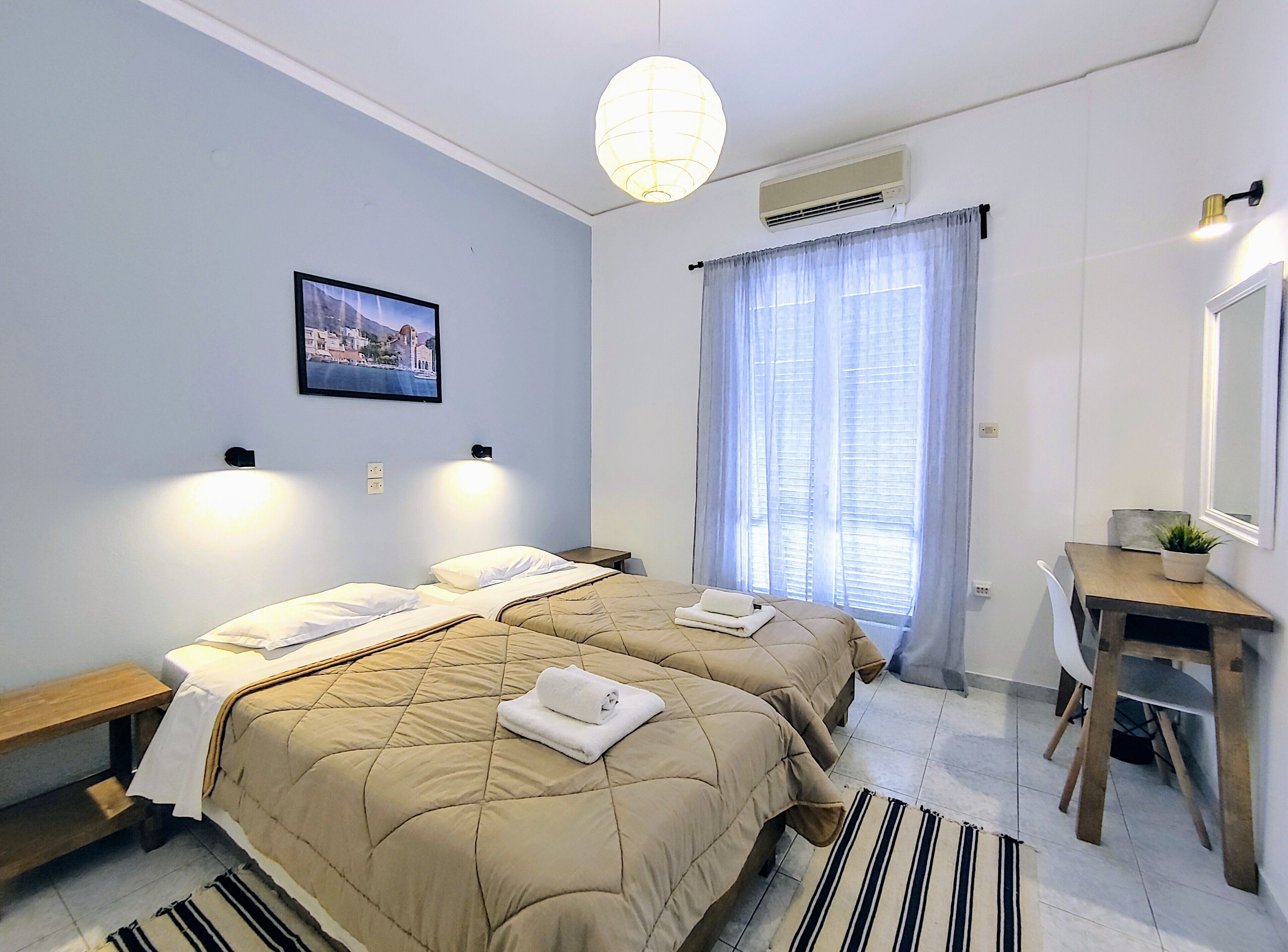 Habitación de hotel con dos camas, un escritorio, una silla, un espejo, un cuadro en la pared y una ventana con cortinas.