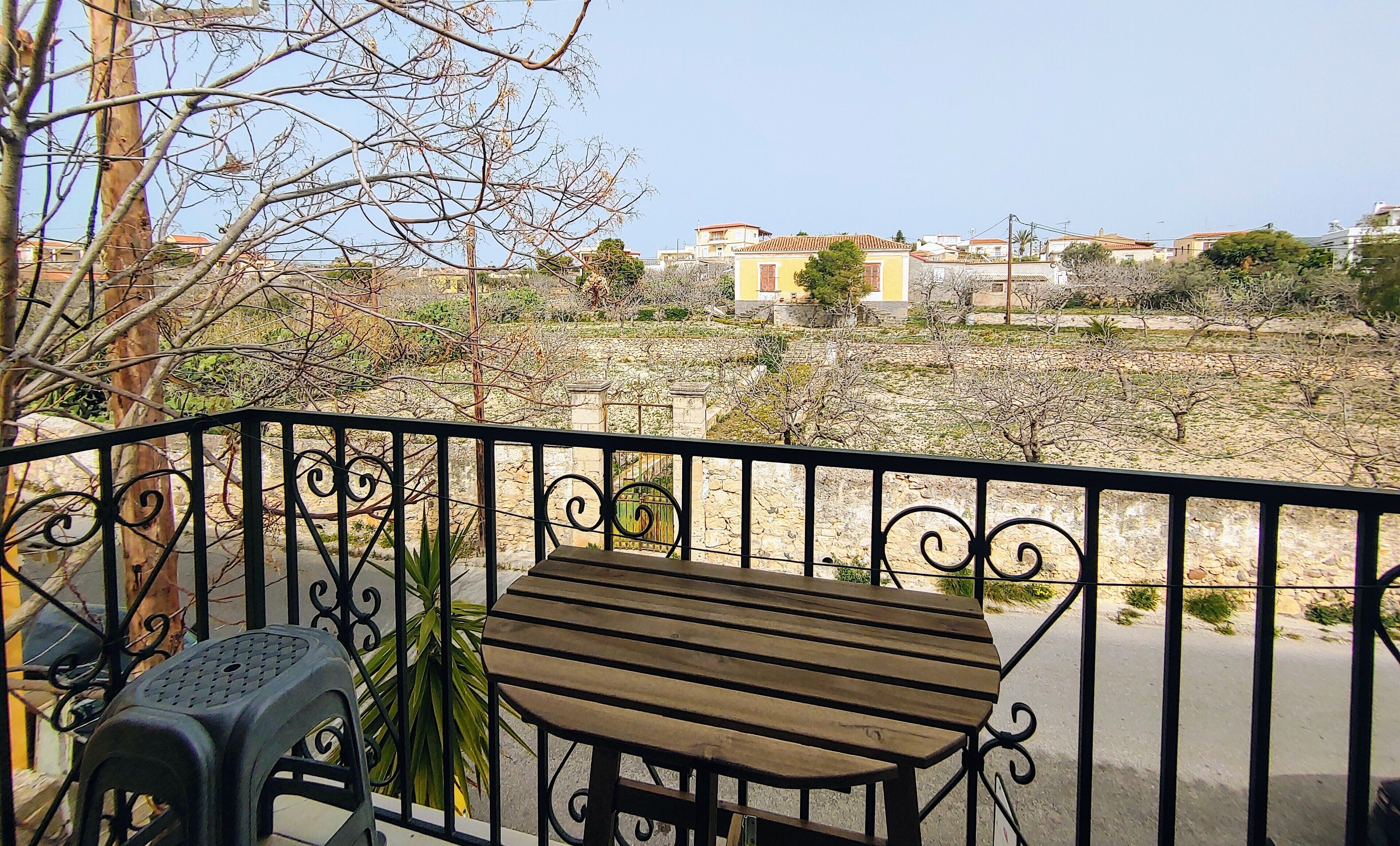 A balcony with a wooden table and chairs, a view of a residential area with houses and trees.