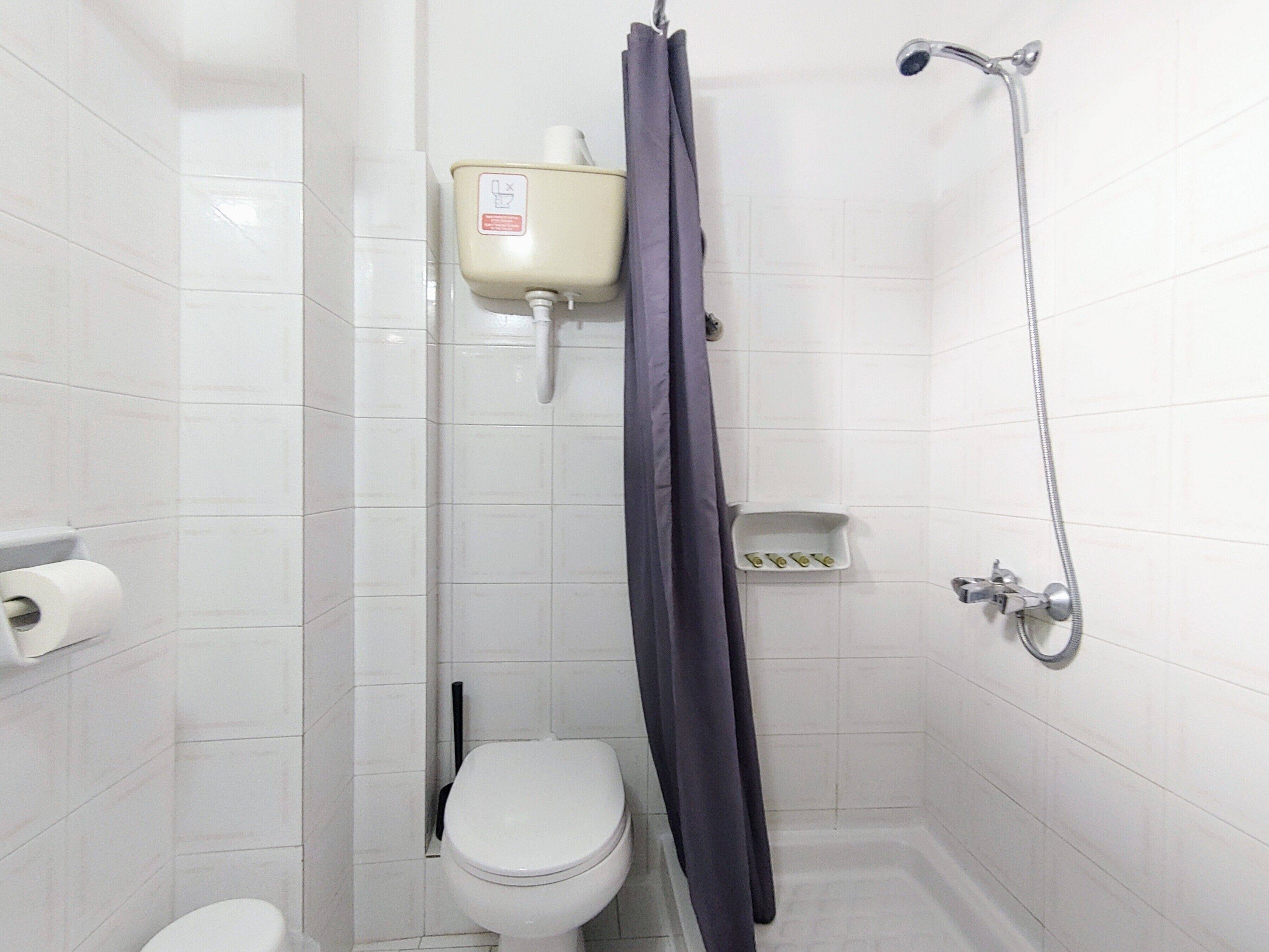 Ein kleines Badezimmer mit weißen Fliesen, ausgestattet mit Toilette, Dusche und Toilettenpapierhalter.