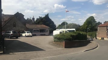A quiet street with a white van parked in a driveway, a flagpole with a flag, and a building with a tiled roof.