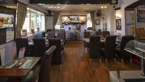 A restaurant with wooden flooring, black leather chairs, and tables. There are posters on the walls and a menu board on the left. - The William IV (Norwich)