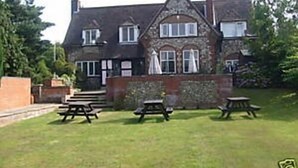 A stone building with a pitched roof and multiple windows, surrounded by a grassy lawn with picnic tables. - The William IV (Norwich)