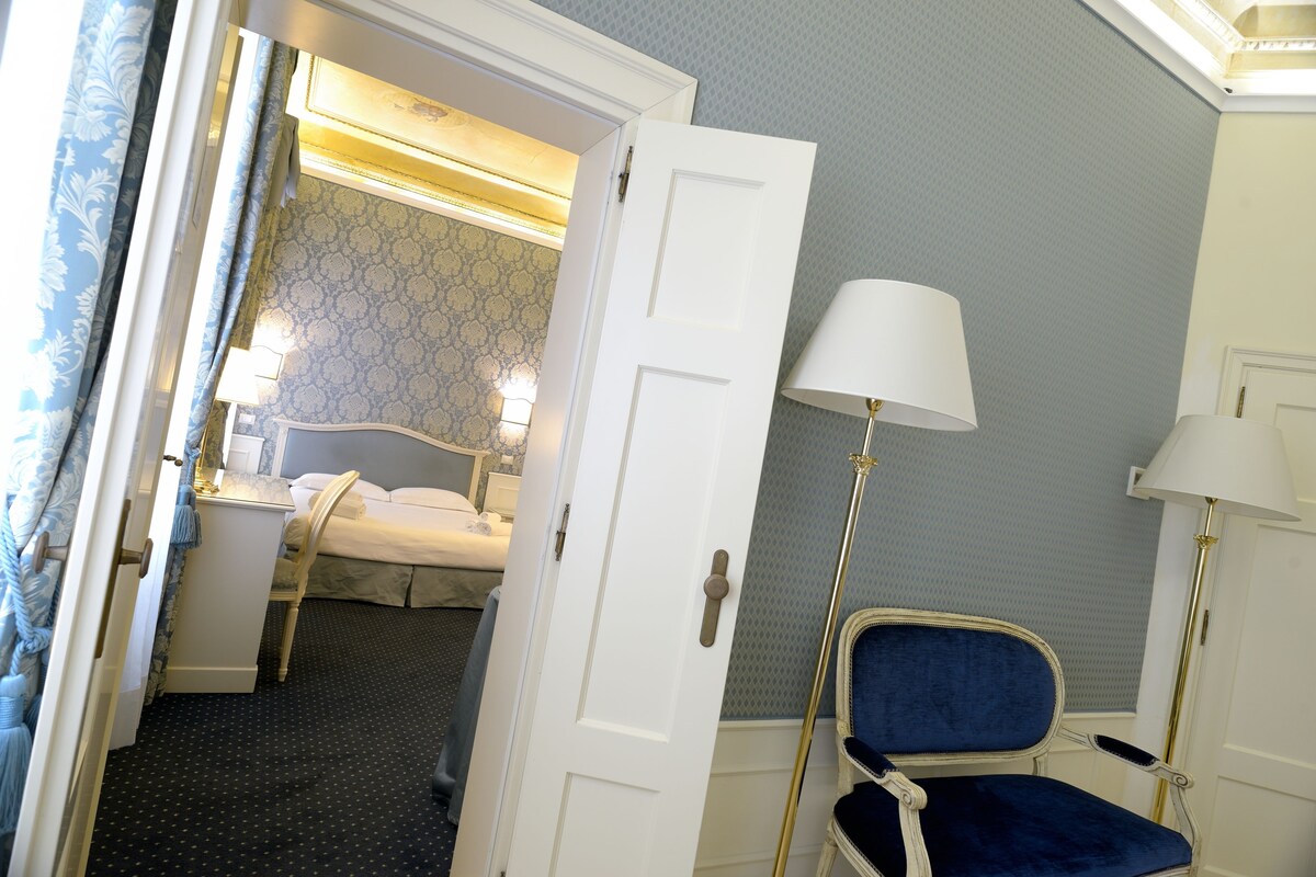 A hotel room with a bed, bedside table, lamp, and a chair.