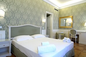 A neatly made bed with white linens and towels, a bedside table with a lamp, and a chair in a room with patterned wallpaper. - Corte Barozzi Venice Suites (Venice)