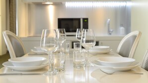 Mesa de jantar posta com pratos brancos, copos e talheres em cozinha moderna com armários brancos e micro-ondas.
