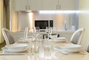 A dining table set with white plates, glasses, and cutlery in a modern kitchen with white cabinets and a microwave.