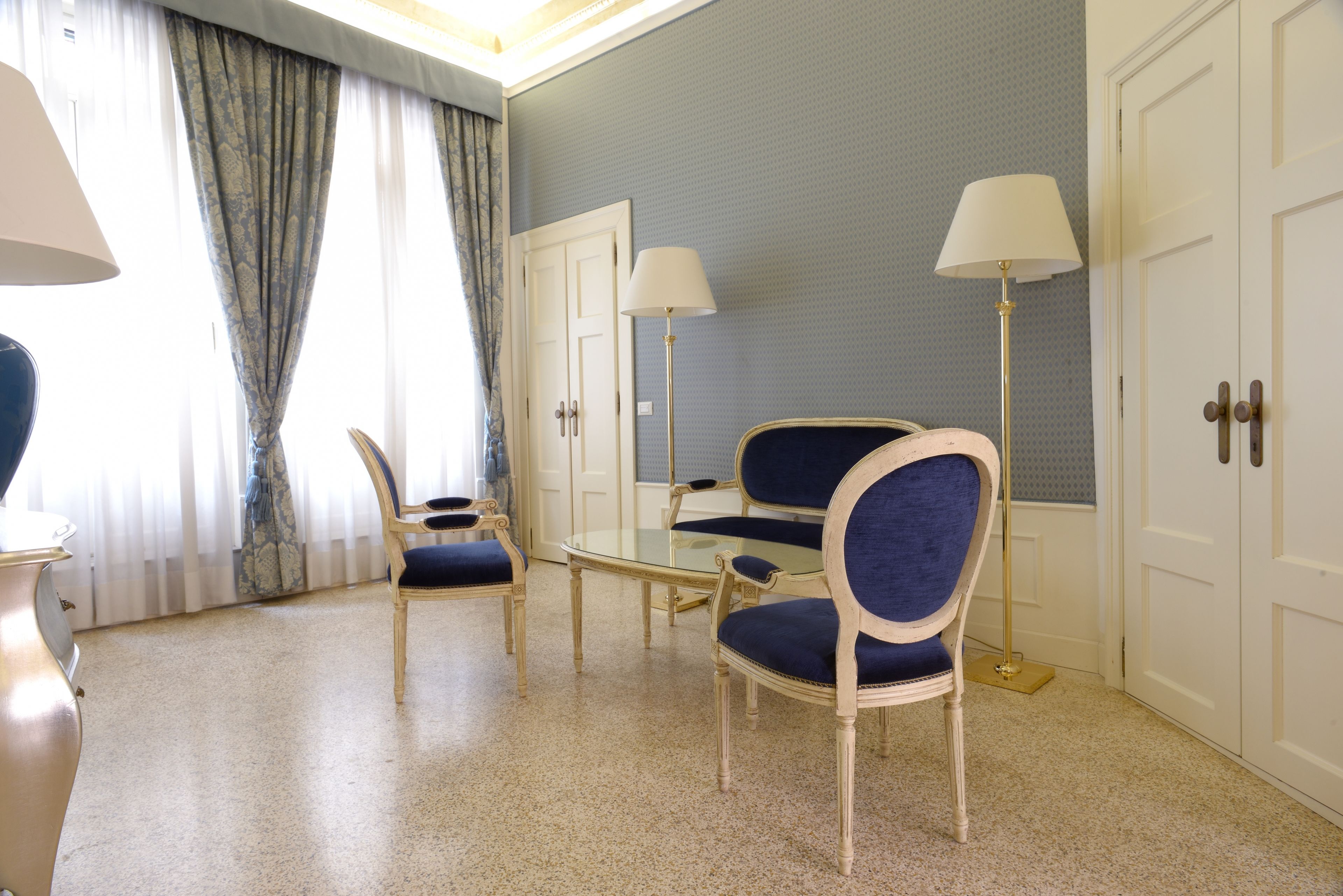 A hotel room with a seating area featuring two chairs and a small table, a large mirror, and a floor lamp.
