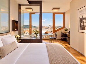 Habitació d'hotel amb un llit gran, un escriptori amb cadira, vista a la ciutat i una finestra amb vista a un pont.