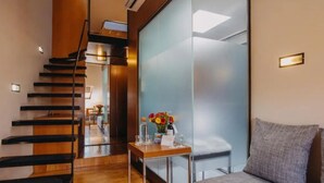 A modern hotel lobby with a wooden staircase, a reception desk with a vase of flowers, and a seating area with a grey sofa. - Wenceslas Square Hotel - Czech Leading Hotels (Prague)