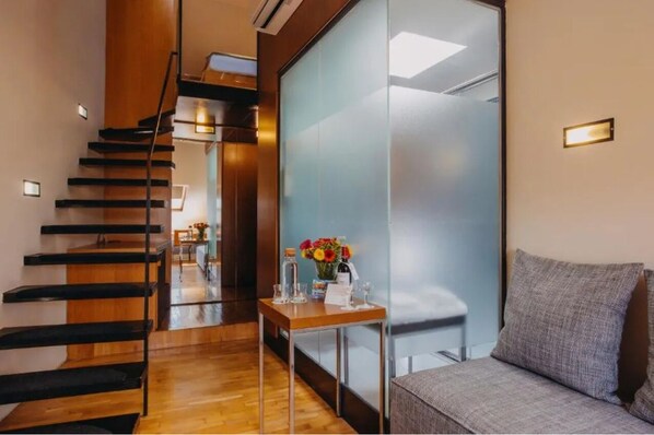 A modern hotel lobby with a wooden staircase, a reception desk with a vase of flowers, and a seating area with a grey sofa. - Wenceslas Square Hotel - Czech Leading Hotels (Prague)