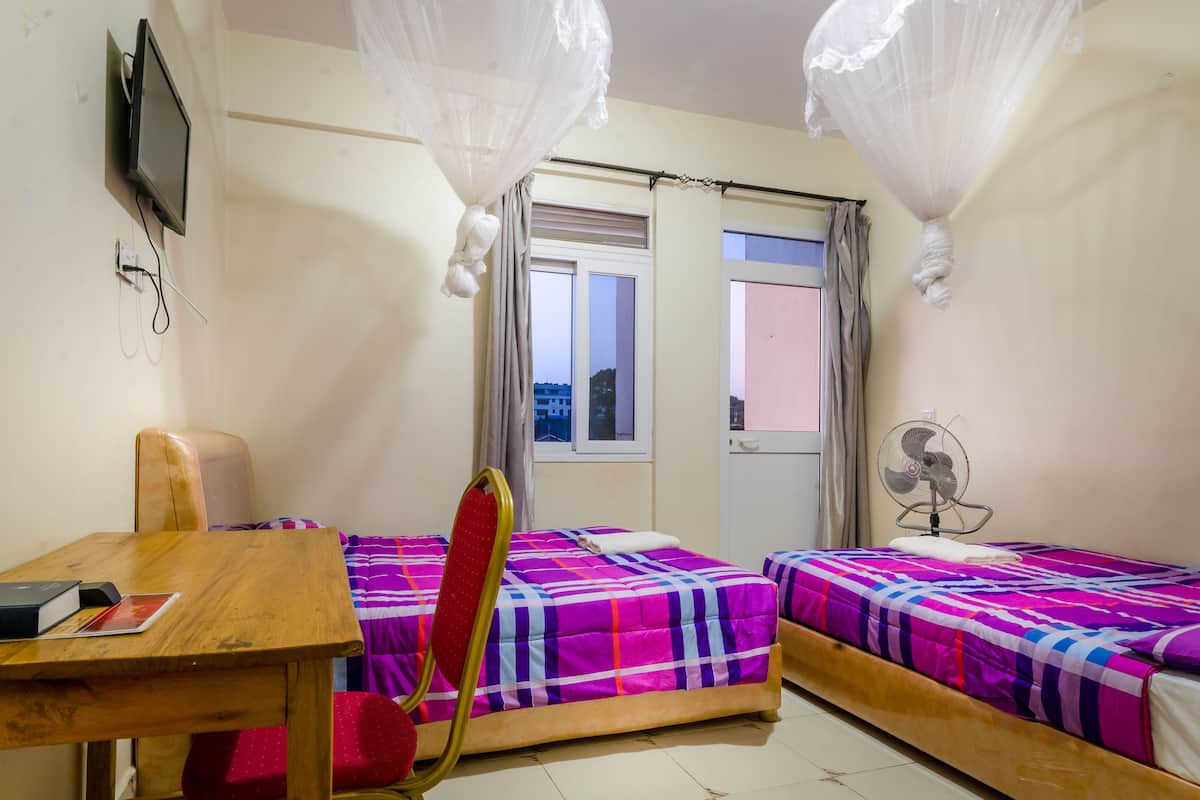 A bedroom with two beds, a desk, a chair, a TV, a window with curtains, and a ceiling fan.