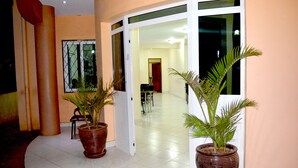 Un pasillo con plantas en macetas, una silla y una puerta que da a un comedor.