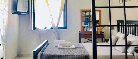 Una habitación con cama, mesita de noche, televisión y ventana con cortinas.