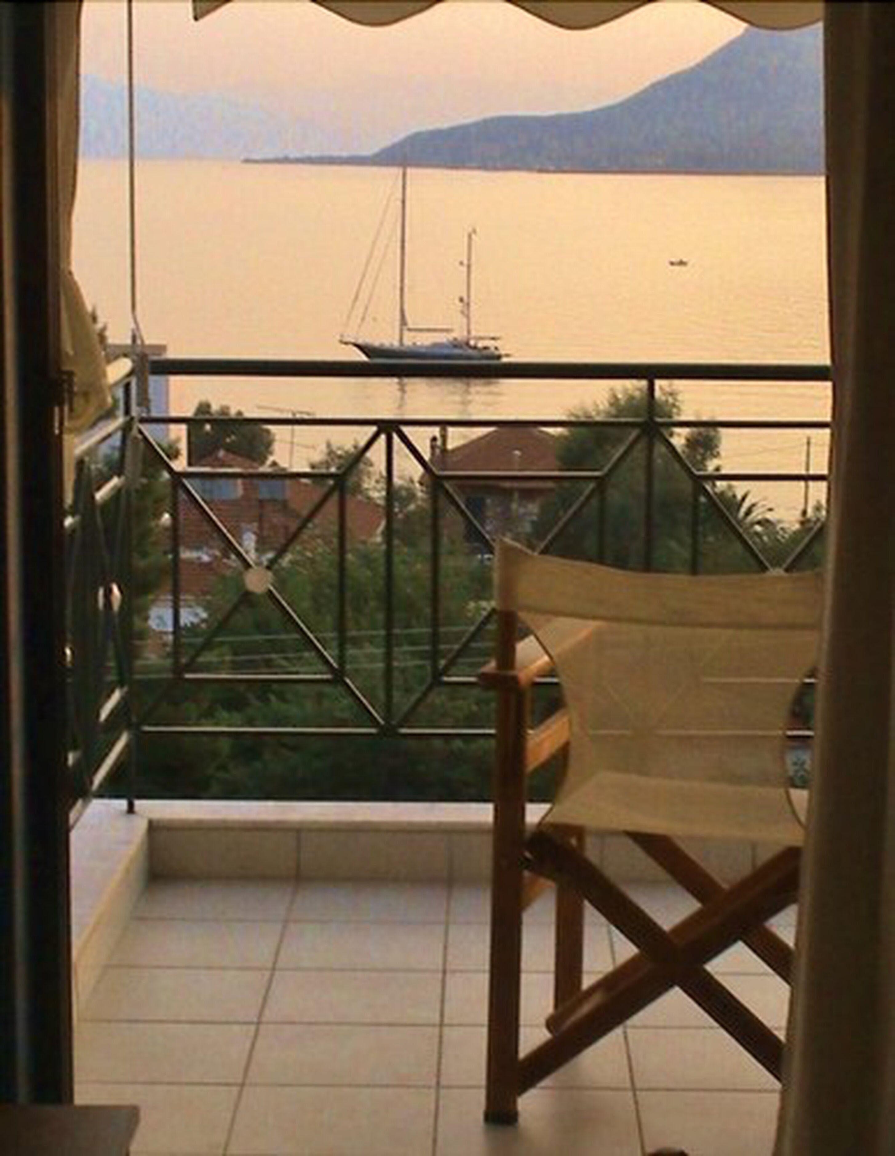 Un balcón con vista a un mar tranquilo y un velero.