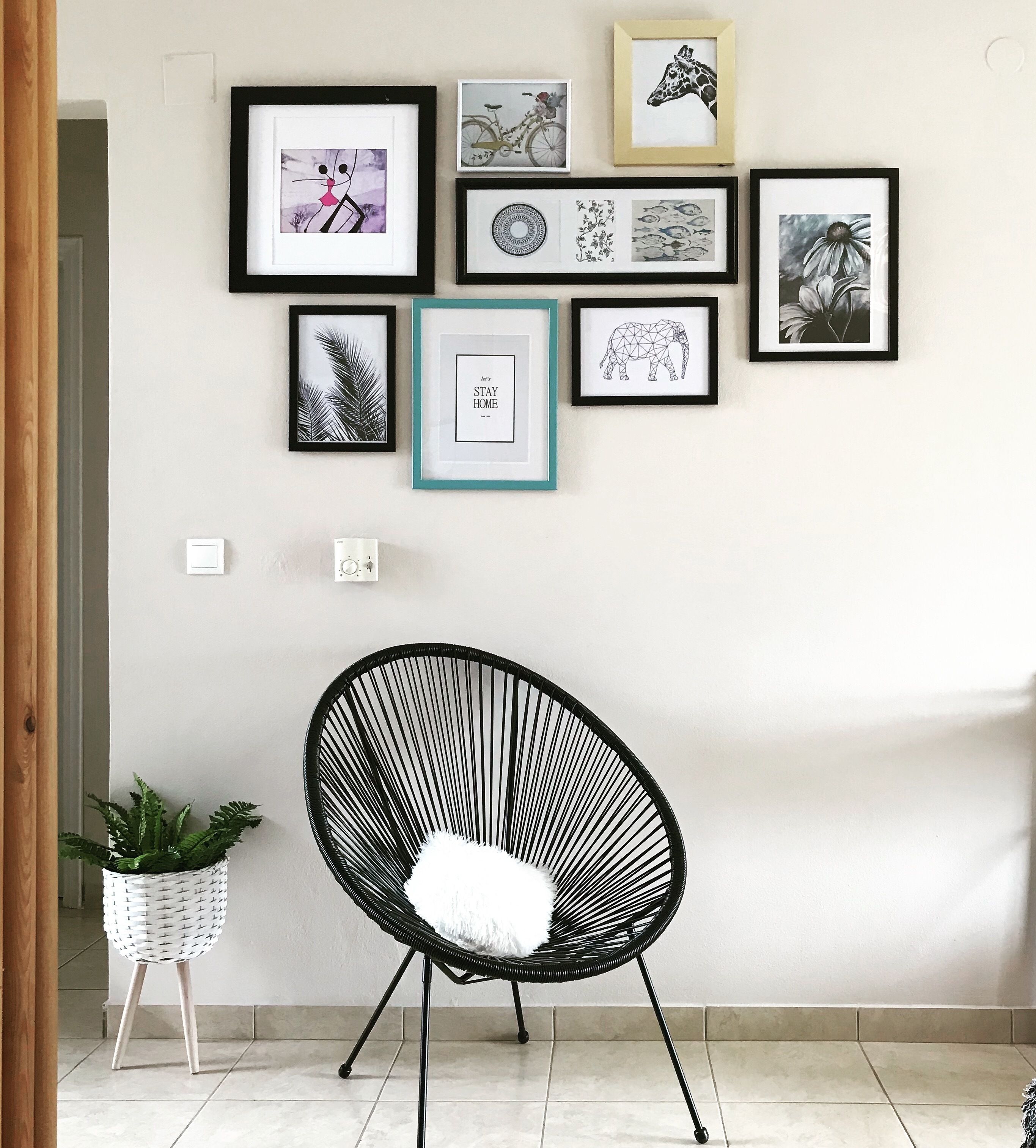 Una habitación con una silla negra, una planta en maceta y una pared decorada con obras de arte enmarcadas.