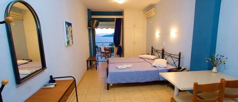 A room with a bed, a desk, a chair, and a table. There is a window with a view of the sea.