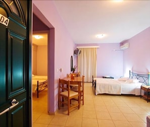 A room with a bed, a desk, and a chair. There is a window with curtains and an air conditioning unit on the wall.
