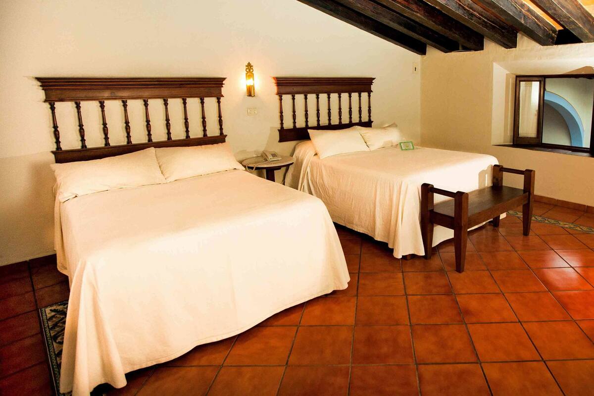A hotel room with two beds, a small table, and a chair.