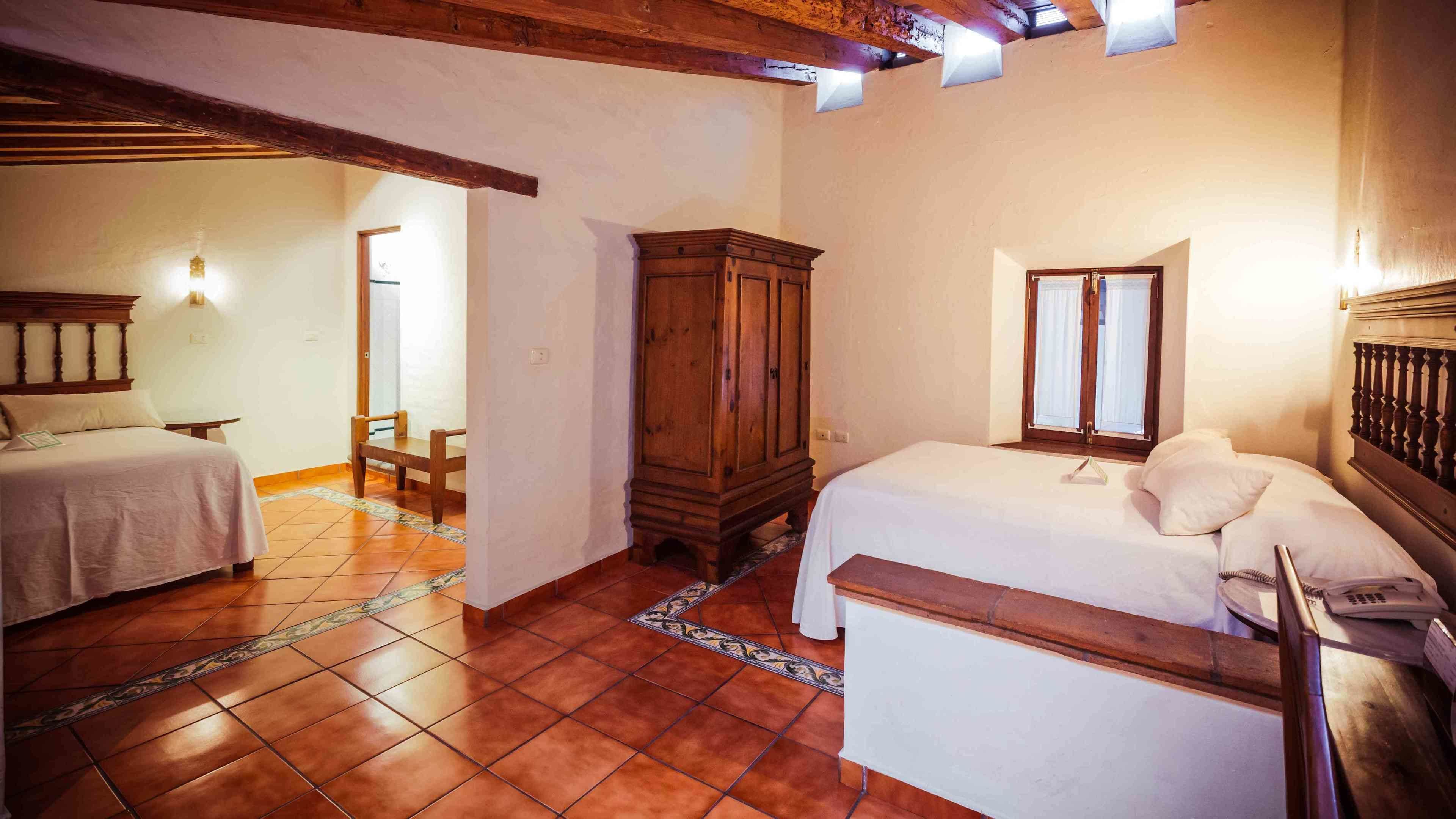 A bedroom with two beds, a wooden wardrobe, a small table, and a window with curtains.