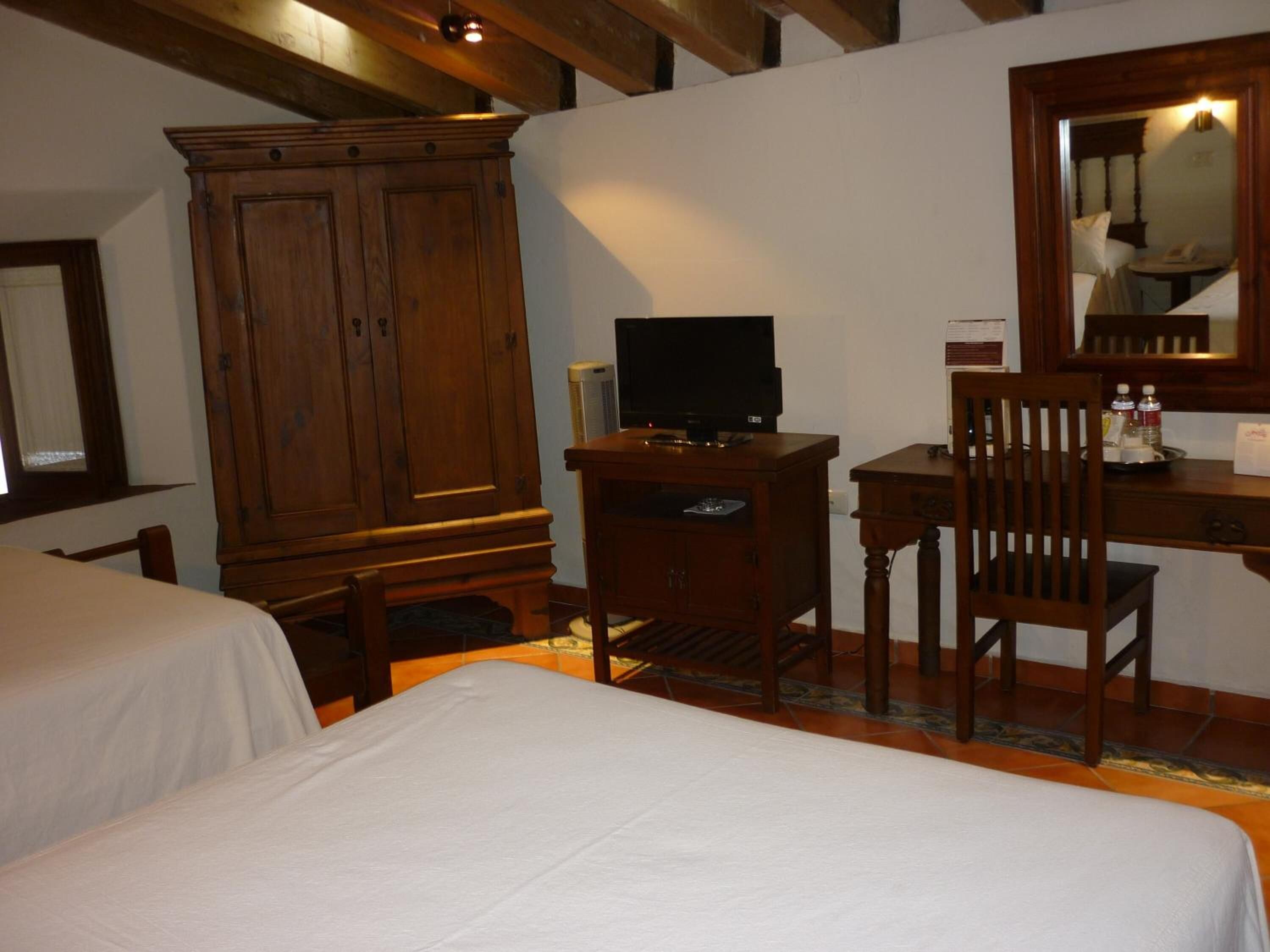 Ein Hotelzimmer mit zwei Betten, einem Holzschrank, einem Schreibtisch mit Stuhl, einem Fernseher und einem Spiegel.