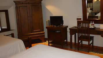 Quarto de hotel com duas camas, um guarda-roupa de madeira, uma escrivaninha com cadeira, televisão e espelho.