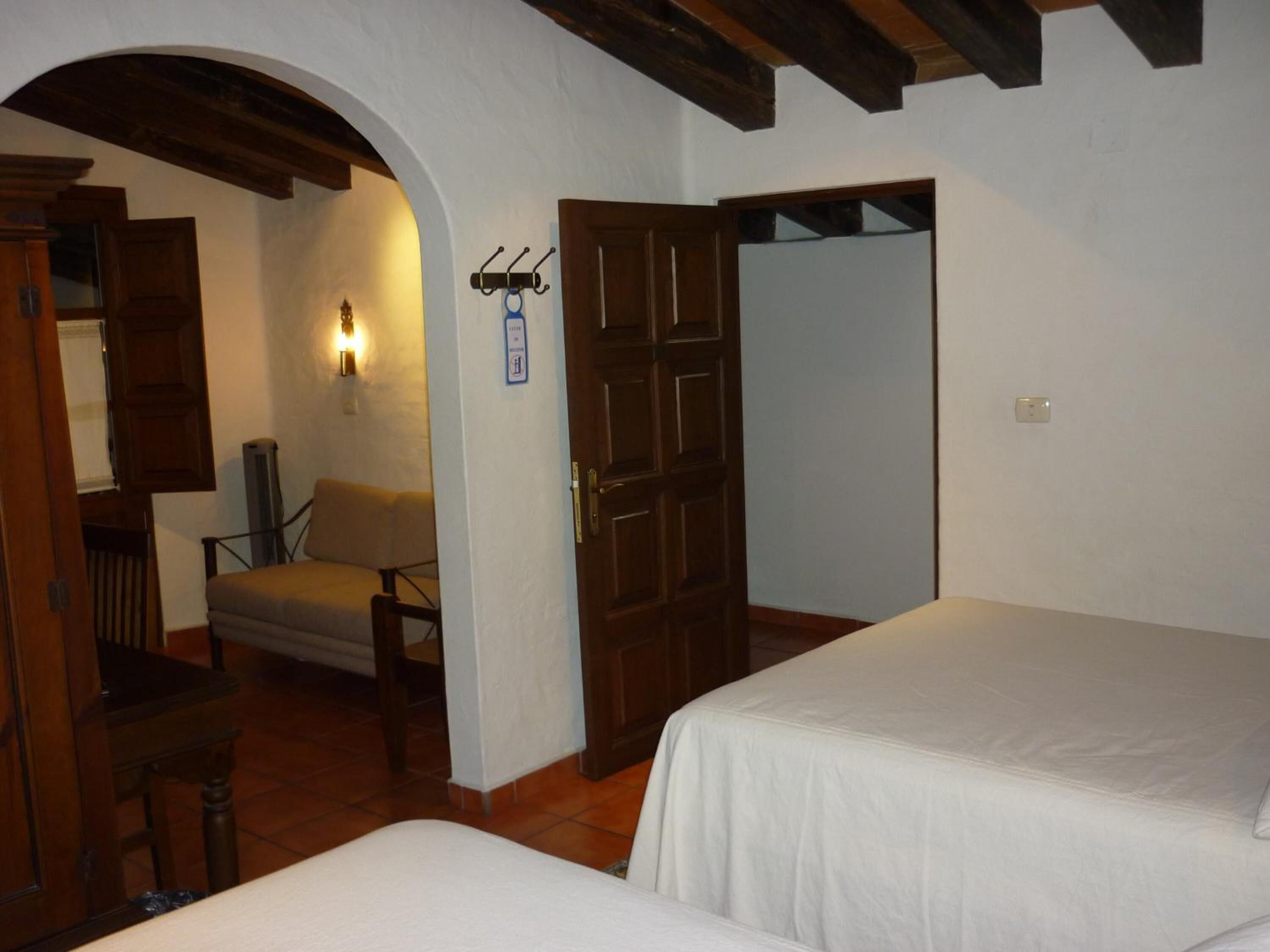 Una habitación con dos camas, una puerta de madera, una silla, una lámpara de pared y una mesita.