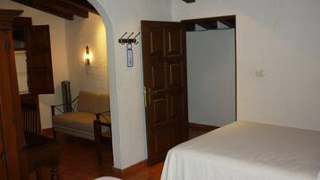 Una habitación con dos camas, una puerta de madera, una silla, una lámpara de pared y una mesita.