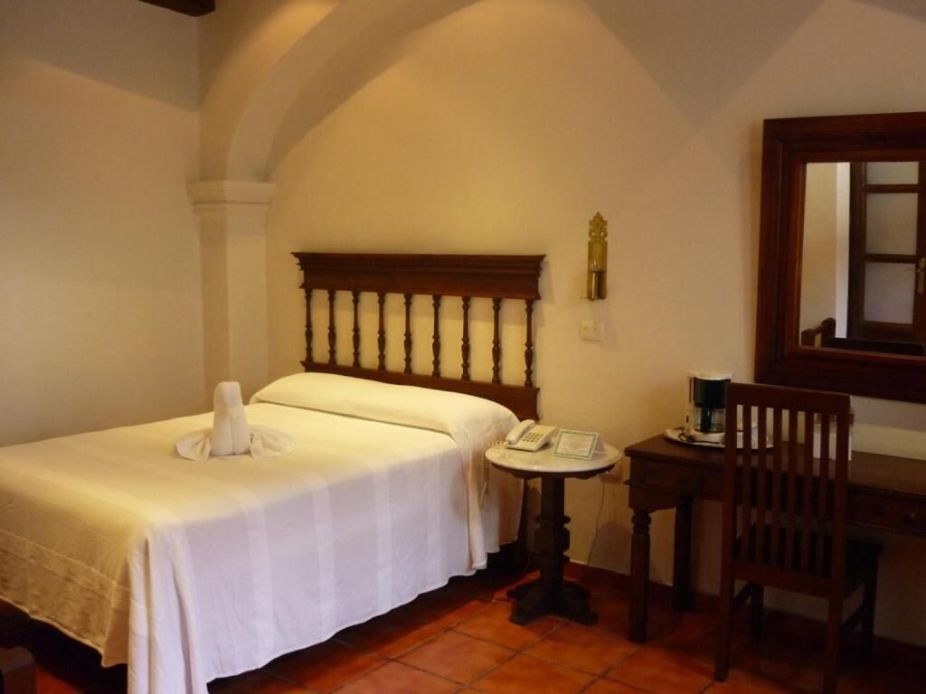 A hotel room with two beds, a small table with a telephone, a chair, and a wooden desk.