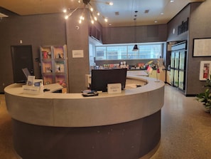Un comptoir d’accueil d’hôtel de forme circulaire, une enseigne indiquant « Marriott Bonvoy », et une vue sur le hall d’entrée, avec une grande fenêtre et une plante.