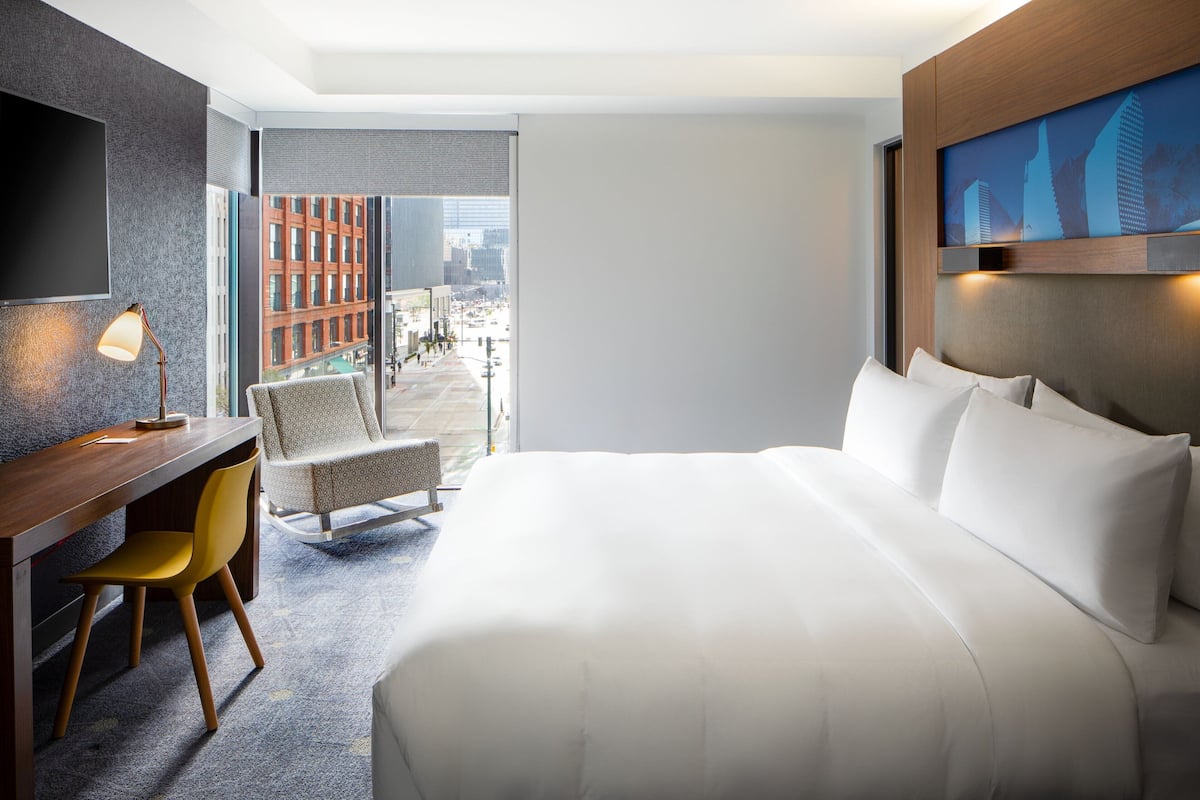 Habitación de hotel con cama, escritorio, silla, televisor y vistas a la ciudad.